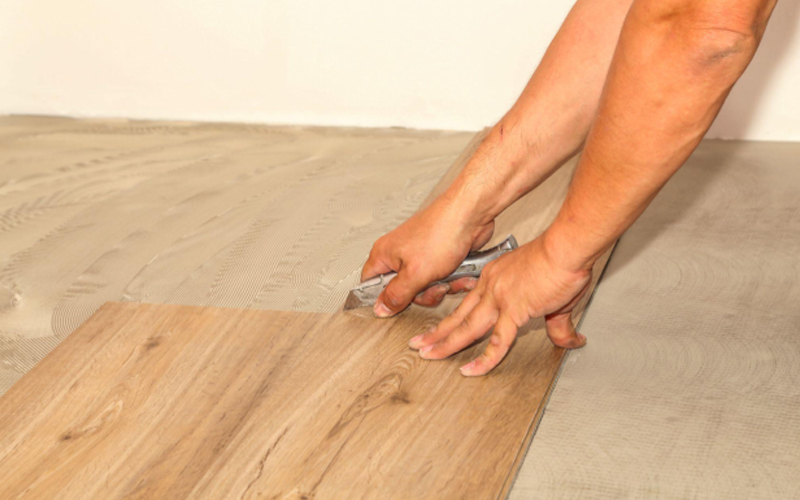 A man is cutting the Luxury Vinyl Plank (LVP) flooring with a utility knife.