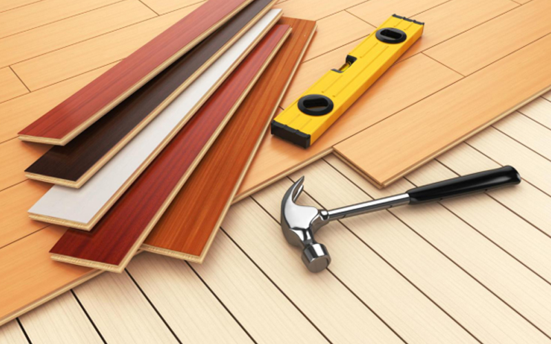 Overlying new flooring on existing surface, with hammer and level as installation tools.