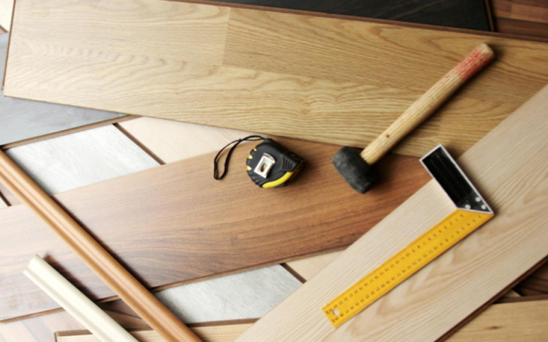 Wood-look floor installation scene with a hammer and leveling instrument.