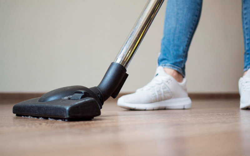 A person in white sneakers using a vacuum cleaner to clean a vinyl floor.