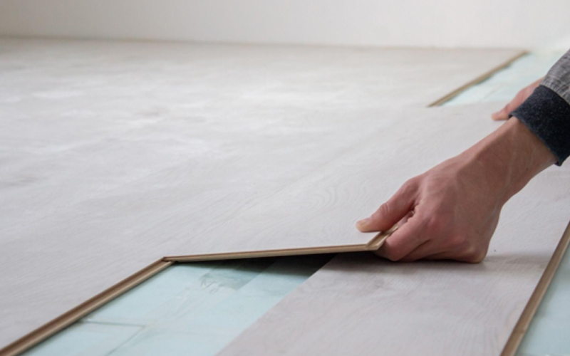 A pair of hands is installing LVT flooring.