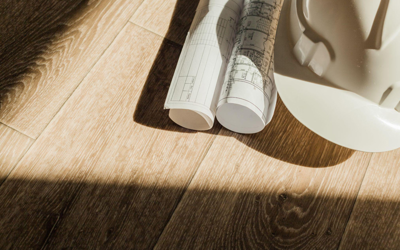  Architectural blueprints and white hard hats on textured WPC wood-grain flooring