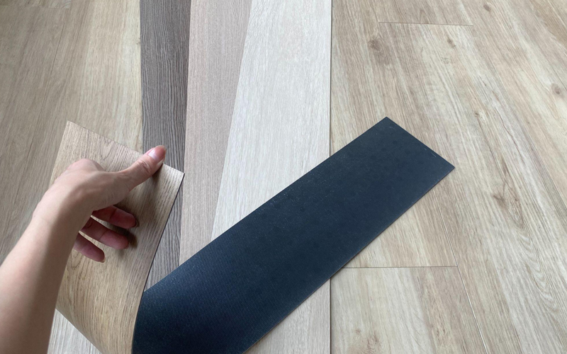 A hand is holding a sample of soft vinyl wood grain flooring, with several different color options displayed.
