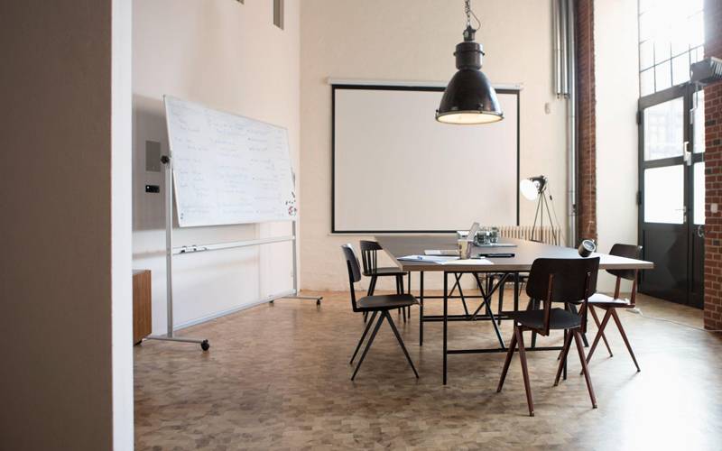 Industrial-style meeting room with conference table, whiteboard, and wooden parquet flooring.