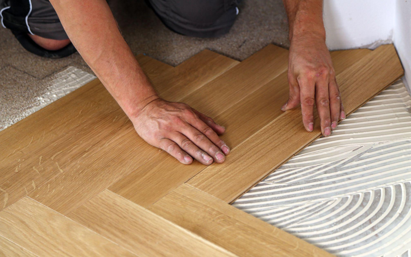 The worker is installing LVT flooring in a herringbone pattern