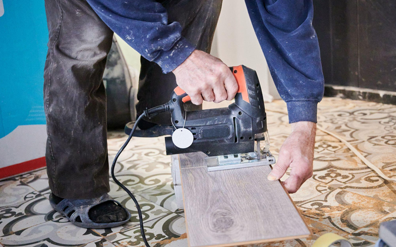 A man is using a jigsaw to cut an LVT plank.