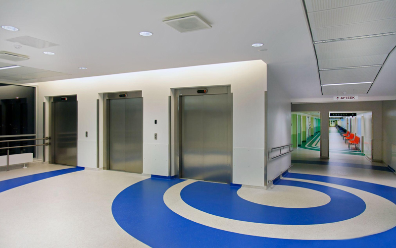 Elevators in a modern hospital atrium with blue circle patterns on homogeneous vinyl flooring.