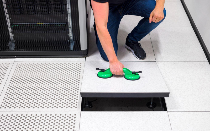 Computer engineer lifting floor tile using vacuum suction cups in a datacenter.