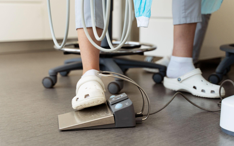 A dentist wearing special shoes presses the dental unit pedal on the floor.