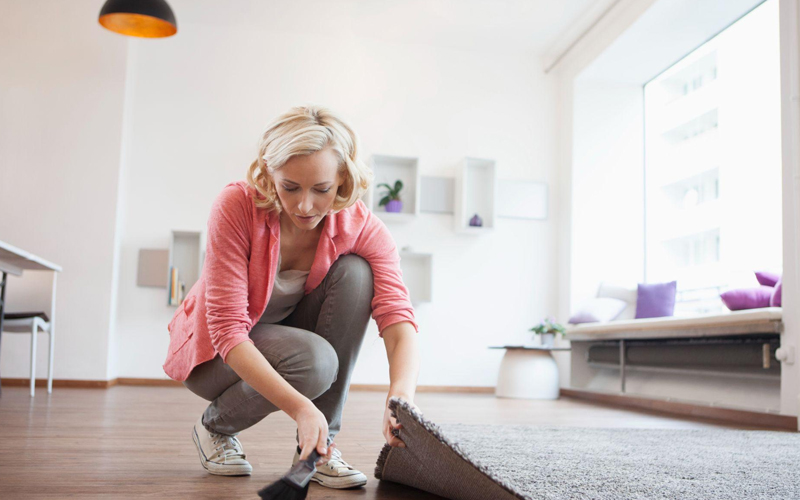 A woman cleaning dust between the floor and carpet